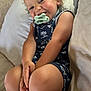 toddler, child, smiling, pacifier, curly_hair, sitting, couch, cushion, indoor, happy, casual_clothing, shorts, sleeveless_shirt, skin, person, portrait, young_child, relaxed, cute, baby