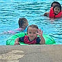 toddler, child, pool, water, float, swimming, life_jacket, green, orange, waving, summer, fun, outdoor, kids, recreation, playful, wet, happy, swimsuit, family