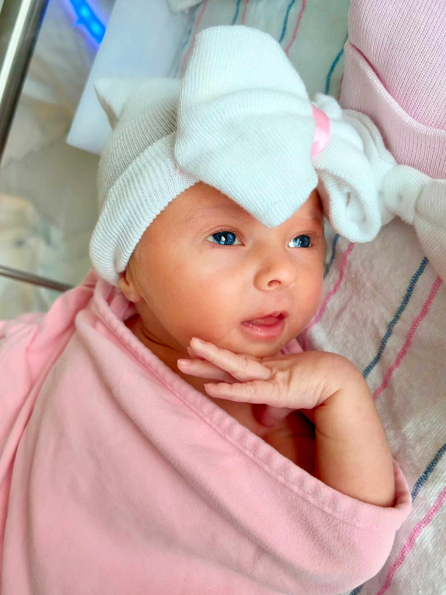 Angelika is registered to the contest to win money with this photo: baby, newborn, infant, hat, bow, swaddle, pink_blanket, hospital_blanket, hand, face, eyes, lips, portrait, closeup, cozy, crib, clothing, blanket_stripes, newborn_cap, cute