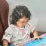 Sanu is registered to the contest to win money with this photo: blanket, book, bracelet, casual_clothing, chair, child, colorful, curly_hair, cute, focused, illustration, indoor, pacifier, person, portrait, reading, relaxed, sea_creatures, toddler, young_child