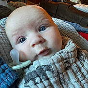 Rune is registered to the contest to win money with this photo: baby, infant, pacifier, blue_eyes, blanket, cloth, face, close_up, indoor, living_room, couch, clock, person, cute, expression, newborn, wrapped, soft_lighting, child, portrait