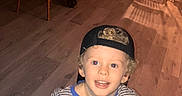 Howard joined the competition — help win amazing prizes! blond, boy, cap, casual_clothing, chairs, child, curly_hair, happy, holding_object, home_interior, indoor, looking_up, person, shadow, smiling, striped_pajamas, table, warm_lighting, wooden_floor, young_child