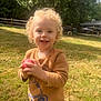 toddler, child, curly_hair, smiling, ball, outdoor, grass, sunlight, sweater, play, happy, person, nature, daylight, fence, casual_clothing, young_child, holding_object, park, greenery