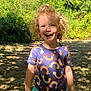 Taryn is registered to the contest to win money with this photo: child, curly_hair, smiling, outdoor, sunlight, shadow, grass, trees, nature, blue_shirt, rainbow_pattern, shorts, happy, young, person, daylight, playful, summer, greenery, park
