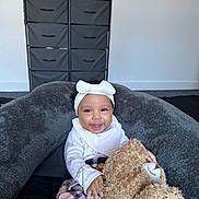 Sienna is registered to the contest to win money with this photo: baby, smiling, teddy_bear, headband, bow, blanket, cushion, infant, child, indoor, cozy, happy, person, plush_toy, clothing, sitting, portrait, furniture, room, soft