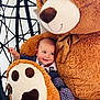 baby, teddy_bear, plush_toy, smiling, child, indoor, cushion, soft_toy, face, happy, cozy, cute, seated, polka_dot, clothing, arm, hand, fabric, chair, comfort