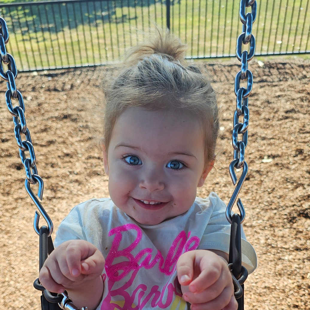 Xhali is registered to the contest to win money with this photo: child, toddler, swing, playground, chains, blue_eyes, smiling, outdoor, daylight, clothing, hair_tied, happy, person, seat, fun, park, casual, cute, face, grip