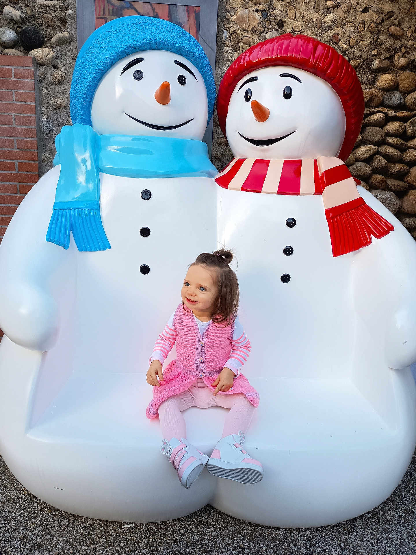 Judith participe au concours pour gagner de l'argent avec cette photo : brick_wall, child, colorful, cute, festive, footwear, happy, hat, holiday, outdoor, pink_clothing, playful, scarf, sculpture, seat, smiling, snowman, stone_wall, toddler, winter_theme