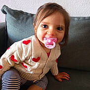 Judith participe au concours pour gagner de l'argent avec cette photo : toddler, child, pacifier, sweater, hearts, striped_pants, couch, indoor, smiling, cute, face, person, seated, cozy, young_child, baby, clothing, hand, hair, light