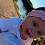 Eliana is registered to the contest to win money with this photo: baby, child, smile, headband, pink, white_clothing, outdoor, sunlight, water, nature, portrait, face, happy, infant, person, closeup, head, skin, cheeks, eyes