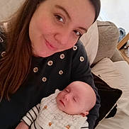 Alex is registered to the contest to win money with this photo: baby, bib, child, clothing, couch, face, furniture, head, home, indoor, long_hair, parent, person, pillow, relaxing, sleeping, smile, striped_clothing, table, woman