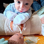 Alex joined the competition — help win amazing prizes! baby, infant, mittens, plush_toy, cushion, floor_mat, person, hand, face, clothing, blue_stripes, indoor, cute, soft_toy, child, closeup, curious, playtime, seated, relaxed