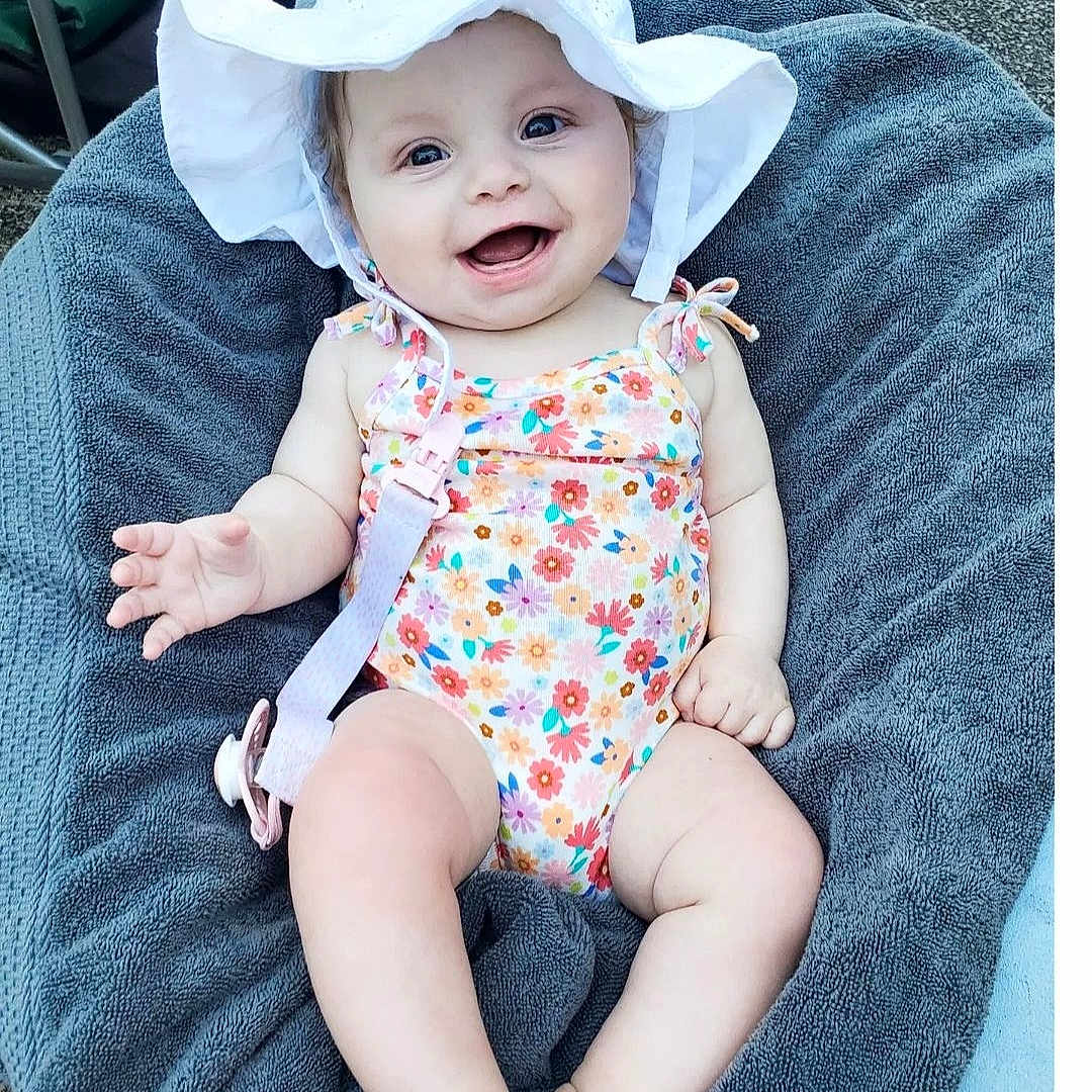 Grace is registered to the contest to win money with this photo: baby, babylaughing, bonnet, cap, clothing, costume, dress, face, furniture, happy, hat, head, pants, person, photography, portrait, quilt, sitting, summer, sunhat