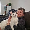 Mojo is registered to the contest to win money with this photo: cat, white_cat, person, man, smiling, couch, indoor, cozy, pet, furry, happy, relaxed, casual_clothing, furniture, home, hand, face, expression, resting, companion