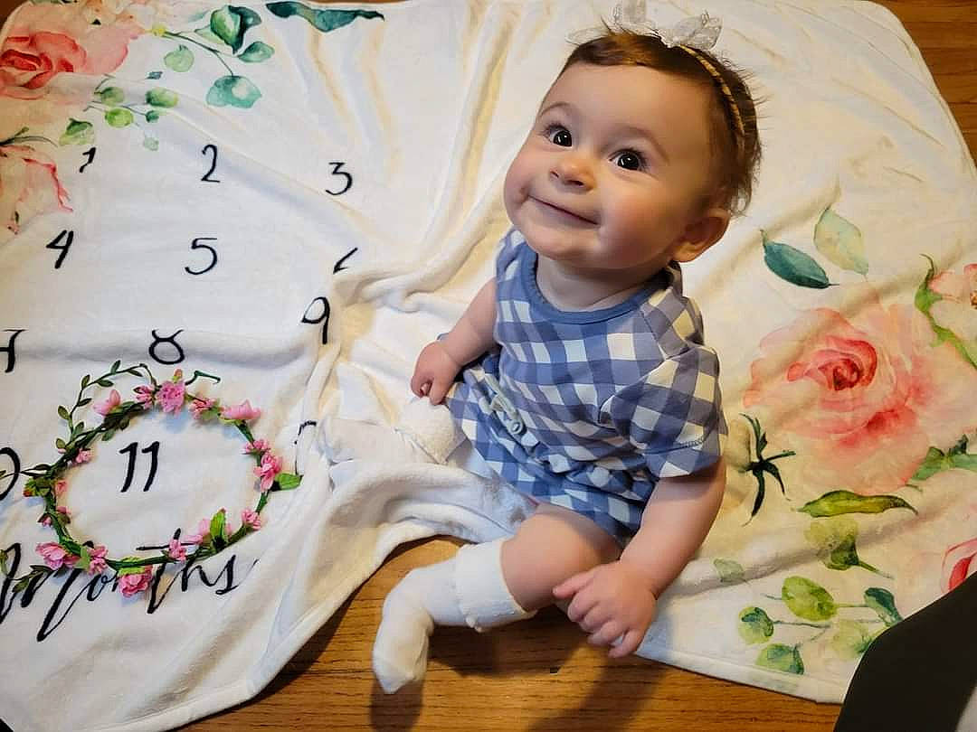 Elyse is registered to the contest to win money with this photo: baby, baby_toddler_clothing, cheek, child, flooring, flower, happy, joy, linens, pattern, person, petal, product, rose, rose_order, sitting, sleeve, smile, t_shirt, textile