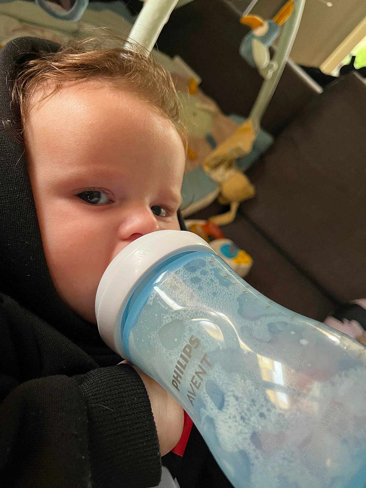 Théo a rejoint le concours — aidez-le/la à gagner de superbes lots ! toddler, child, baby_bottle, foam, philips_avent, black_hoodie, indoor, face, hand, curly_hair, couch, toy, window, living_room, person, close_up, hydration, young_child, casual_wear, bottle_feeding