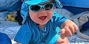 Théo a rejoint le concours — aidez-le/la à gagner de superbes lots ! baby, beach, blanket, blue_hat, child, clothing, cute, face, feet, happy, headwear, infant, outdoor, playful, sitting, smiling, summer, sunglasses, sunlight, tent