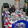 cat, black_cat, kitten, animal, pet, face, eyes, pointed_ears, whiskers, indoors, household, bottled_water, water_bottles, packaging, supplies, table, storage, spray_can, boxes, portrait