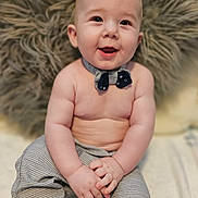 Roman is registered to the contest to win money with this photo: baby, child, smiling, bow_tie, pants, sitting, hands, face, cute, happy, fluffy_pillow, indoor, skin, portrait, infant, clothing, young, closeup, expression, person