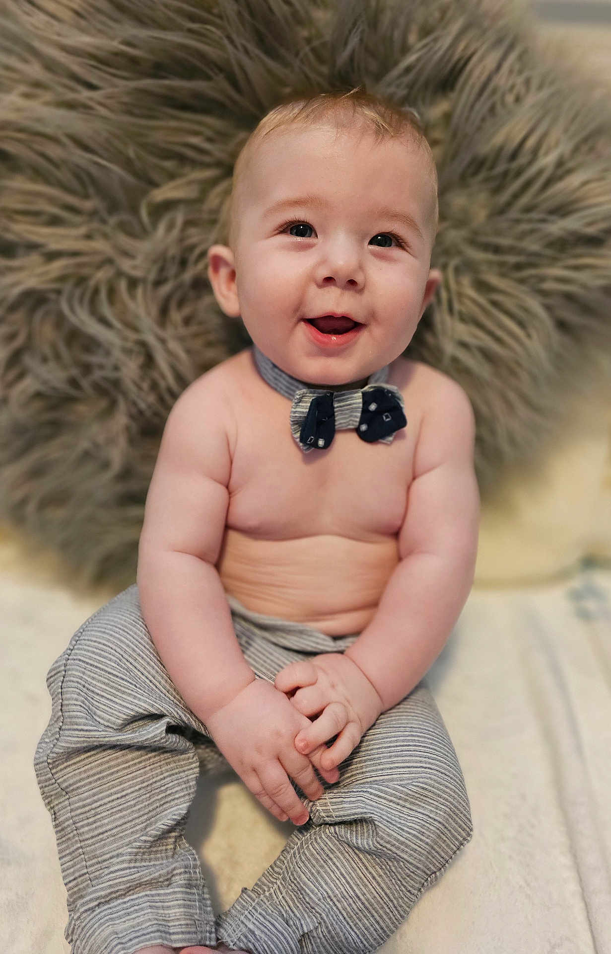 Roman is registered to the contest to win money with this photo: baby, child, smiling, bow_tie, pants, sitting, hands, face, cute, happy, fluffy_pillow, indoor, skin, portrait, infant, clothing, young, closeup, expression, person
