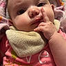 April is registered to the contest to win money with this photo: baby, infant, child, portrait, lying_down, blanket, hood, pink_clothing, bib, finger, hand, face, eyes, nose, curious, indoors, cozy, close_up, textile, photography