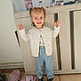 basket, cabinet, cardigan, child, floor_tiles, framed_photo, happy, home_interior, indoor, person, photograph, pigtails, playful, portrait, slippers, smile, sneakers, striped_pants, toddler, toys