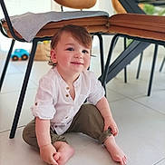 Andrea participe au concours pour gagner de l'argent avec cette photo : toddler, child, smiling, sitting, barefoot, white_shirt, olive_pants, rolled_cuffs, indoor, floor, tile, chair, table, toy_car, cute, happy, curly_hair, baby, person, home