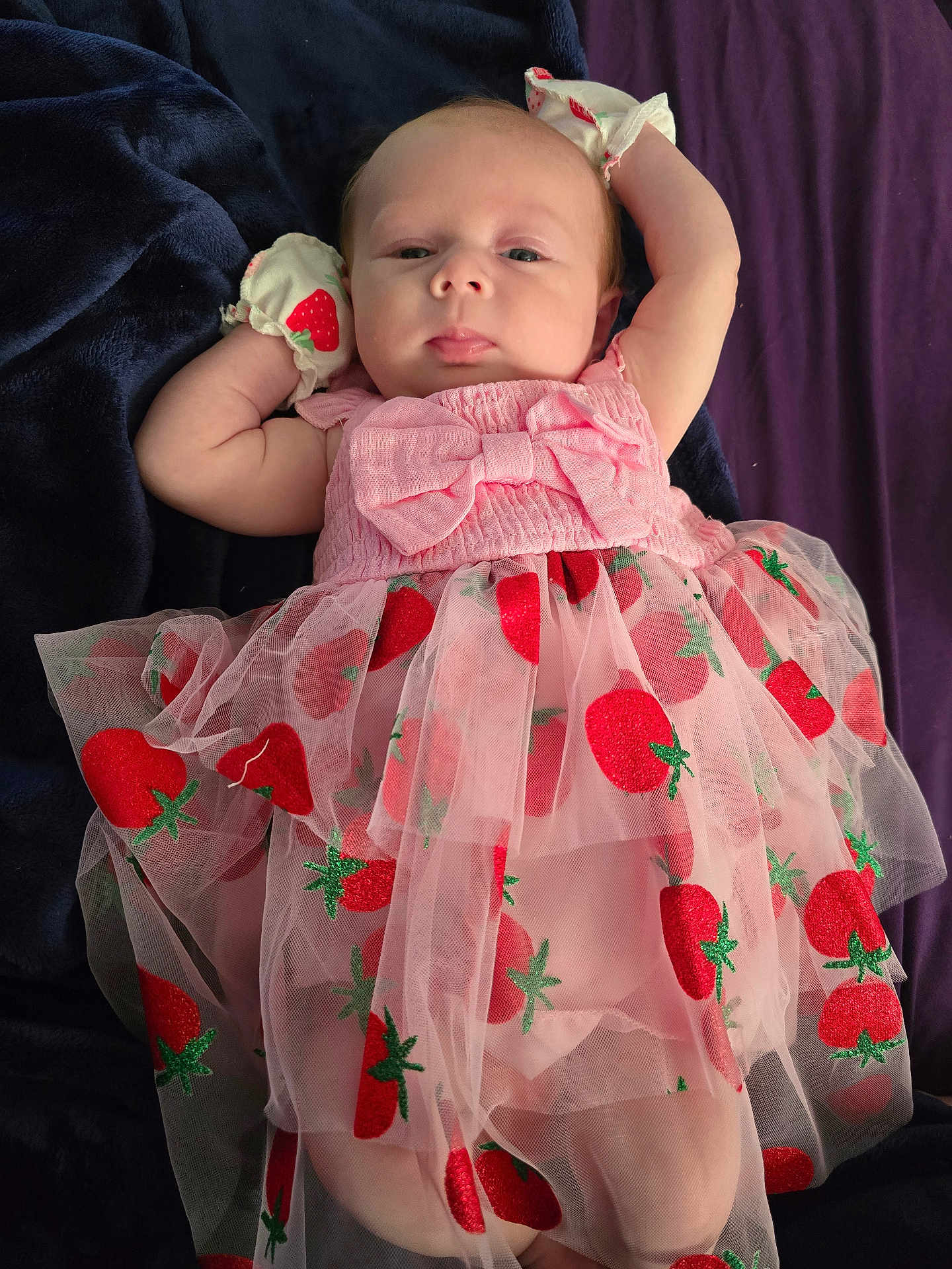 Terrilyn is registered to the contest to win money with this photo: baby, infant, pink_dress, strawberry_pattern, mittens, blanket, lying_down, cute, child, portrait, soft_fabric, relaxed, indoors, closeup, tulle, clothing, person, newborn, face, sleepwear