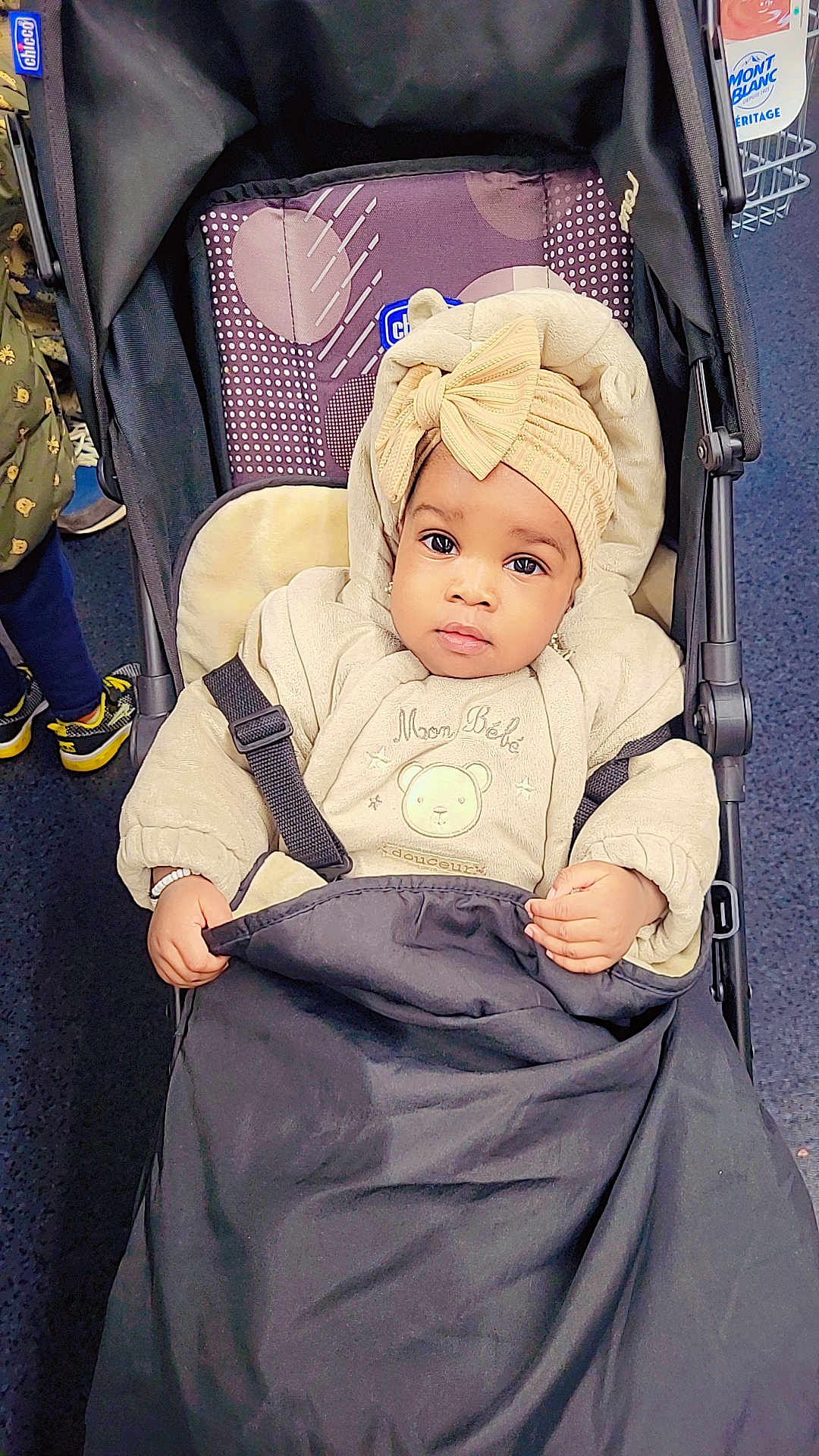 Saran Ballo a rejoint le concours — aidez-le/la à gagner de superbes lots ! baby, stroller, child, clothing, headwrap, bow, blanket, indoor, person, face, warm_clothing, seat, pattern, hand, footwear, floor, fabric, curious, black, beige