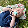 Archie is registered to the contest to win money with this photo: baby, pacifier, blanket, grass, outdoor, infant, clothing, hands, face, head, blue_eyes, buttoned_shirt, nature, lying_down, cute, skin, person, soft_focus, floral_pattern, daylight