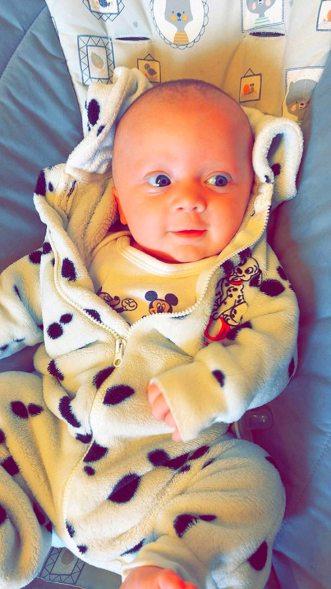 Archie is registered to the contest to win money with this photo: baby, infant, onesie, dalmatian_pattern, cute, child, clothing, face, blue_eyes, soft_fabric, patterned_cushion, animal_print, smiling, lying_down, indoor, young_child, cozy, zipper, hooded_outfit, cute_expression
