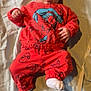 baby, infant, child, spiderman_outfit, red_clothing, tongue_out, blanket, lying_down, white_socks, pacifier, carpet, cute, playful, indoors, soft_lighting, portrait, young_child, face, hands, feet