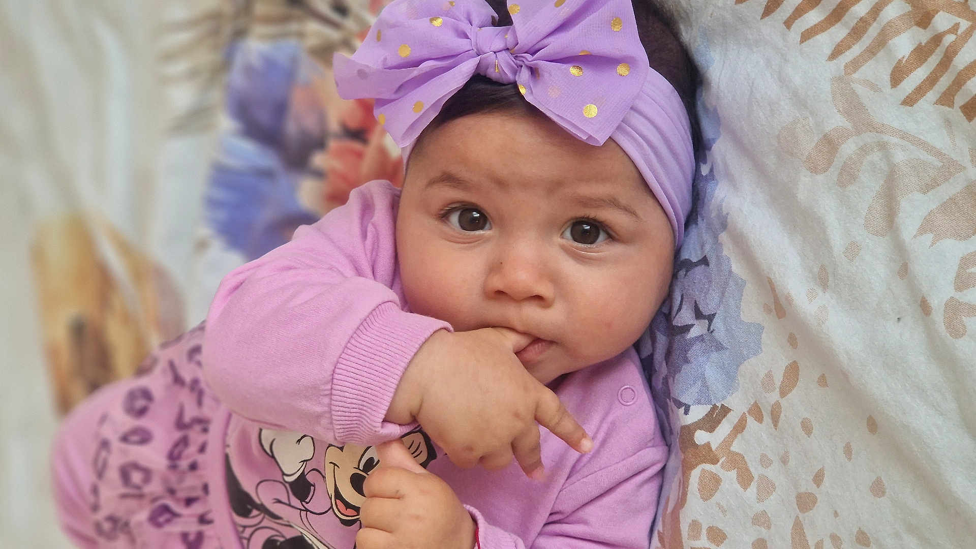 Klara participe au concours pour gagner de l'argent avec cette photo : baby, child, infant, purple_bow, pink_clothing, minnie_mouse, hand, fingers, face, eyes, blanket, pattern, lying_down, cute, portrait, indoors, headband, sleeve, expression, soft_light