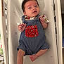 baby, crib, romper, blue_clothing, red_pocket, infant, bedding, stars, moon, soft, cute, smile, lying_down, indoor, child, newborn, face, skin, hair, peaceful