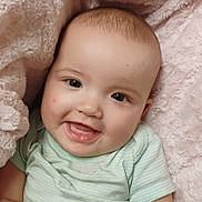 Elena is registered to the contest to win money with this photo: baby, smiling, face, child, infant, blanket, soft_texture, clothing, green_onesie, cute, happy, portrait, head, skin, cheeks, eyes, mouth, teeth, indoor, closeup