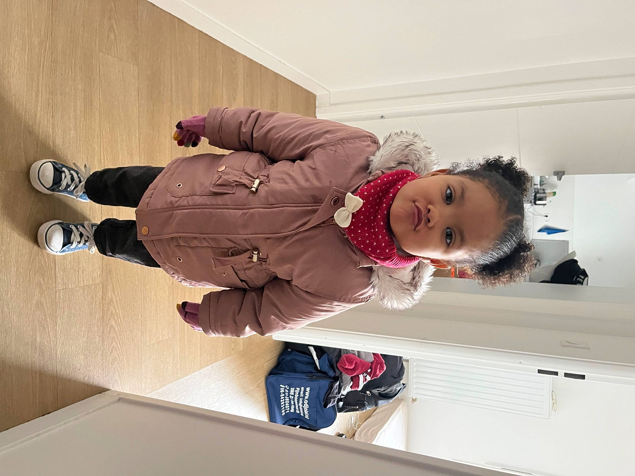 Arya participe au concours pour gagner de l'argent avec cette photo : baby_toddler_clothing, cabinetry, child, comfort, flooring, hardwood, knee, outdoor_shoe, person, room, sitting, sleeve, smile, toddler, walking_shoe, wood