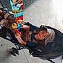 Levi joined the competition — help win amazing prizes! child, stroller, toy, fishing_rod, camouflage_pants, headscarf, smiling, chalk_drawings, concrete, outdoor, footwear, casual_clothing, person, wheel, handle, playful, young, seated, happy, daylight