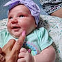 baby, infant, smiling, headband, purple, hand, finger, clothing, green_shirt, floral, fabric, closeup, cute, chubby, skin, person, indoors, portrait, happy, newborn