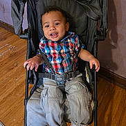 Cayden joined the competition — help win amazing prizes! toddler, child, stroller, plaid_shirt, cargo_pants, shoes, smile, indoors, wooden_floor, wall, seatbelt, black_stroller, happy, person, young_child, casual_clothing, cute, baby, sitting, portrait