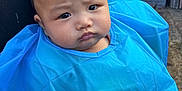 Archie is registered to the contest to win money with this photo: baby, child, blue_cape, face, furrowed_brow, person, black_shirt, outdoor, plastic, cape, head, expression, portrait, curious, young_child, human, skin, hair, reflection, background