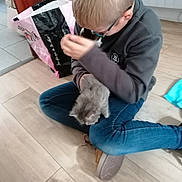 Mistigris a rejoint le concours — aidez-le/la à gagner de superbes lots ! boy, kitten, cat, child, glasses, floor, wooden_floor, jeans, sitting, indoor, bag, chair, sweatshirt, pet, cute, young, home, casual, holding, animal