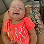 Wrenlee is registered to the contest to win money with this photo: baby, infant, smile, onesie, pink, tattoo, tattooed_leg, lap, couch, living_room, water_bottle, pillow, close_up, face, hand, arm, skin, person, happy, text_on_shirt