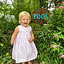 child, toddler, dress, barefoot, garden, flowers, greenery, plants, tree, wooden_sign, outdoor, happy, smiling, nature, summer, daylight, leaves, path, wood, pink