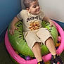 child, boy, inflatable, pool, kiwi_ring, ball_pit, indoor, casual_clothing, shorts, tshirt, sneakers, smile, playful, corner, wall, artificial_grass, floor, toy, fun, relaxing
