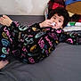 child, bed, blanket, clothing, curly_hair, face, furniture, indoor, looking_at_camera, nasa, person, pillow, plaid, pose, shirt, sleeve, toy, wall, young, youth