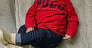 Asher is registered to the contest to win money with this photo: baby, child, smiling, red_shirt, hat, beige, polo, jeans, socks, couch, furniture, indoor, cute, happy, portrait, person, sitting, infant, young_child, casual_clothing