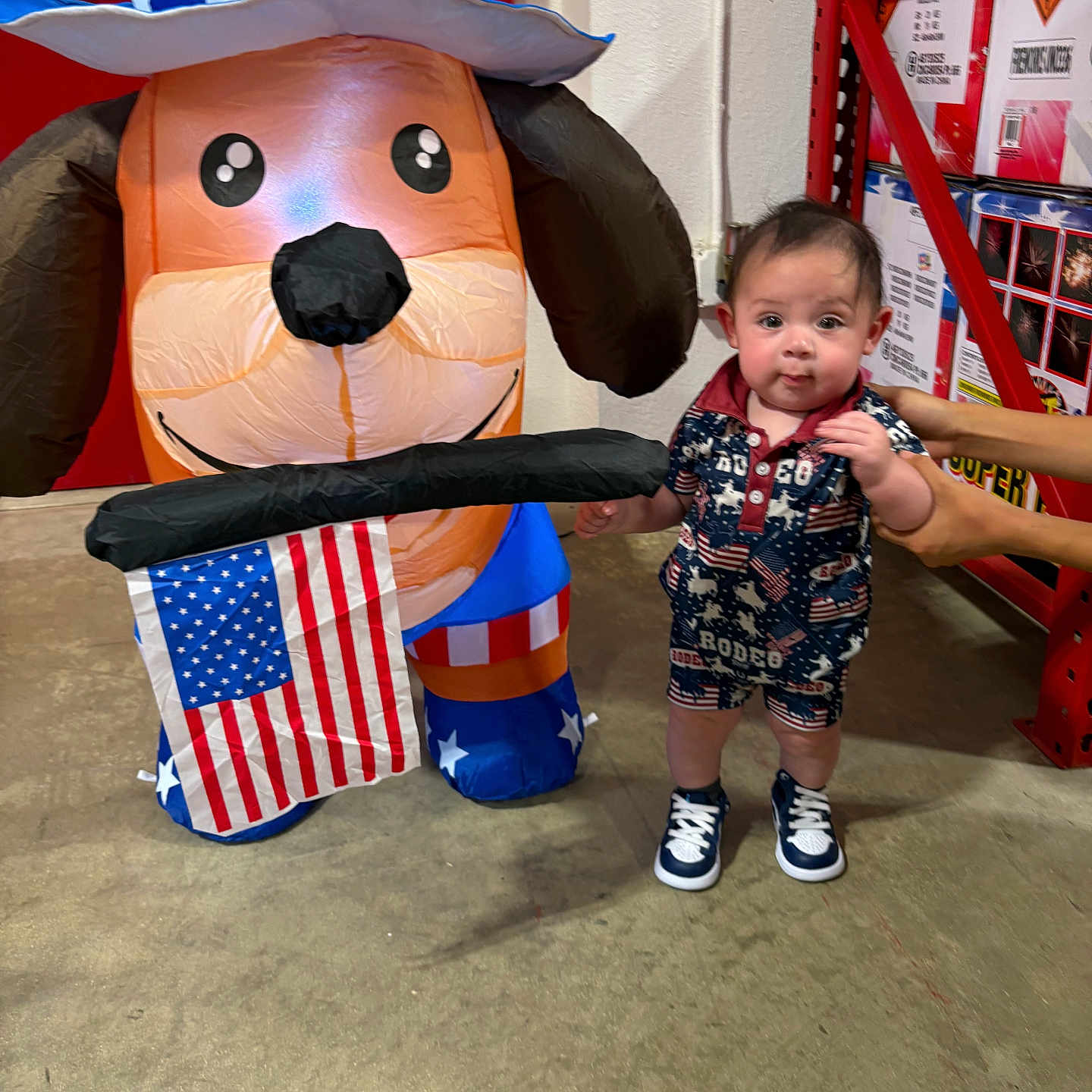 Cruz Carlos joined the competition — help win amazing prizes! toddler, child, inflatable, dog, american_flag, patriotic, hat, warehouse, concrete_floor, boxes, red_shelf, hands, clothing, sneakers, standing, face, person, indoor, toy, celebration