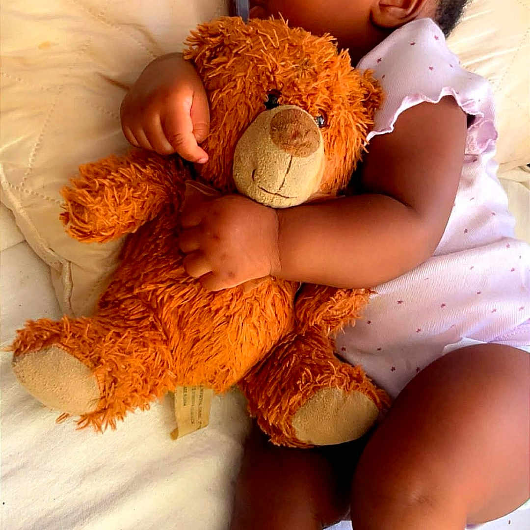 London joined the competition — help win amazing prizes! baby, infant, sleeping, teddy_bear, stuffed_animal, cuddling, bed, blanket, pajamas, dress, portrait, indoors, peaceful, resting, closed_eyes, baby_hand, baby_arm, baby_legs, soft_lighting, cozy