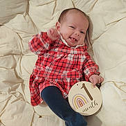 Naëlya participe au concours pour gagner de l'argent avec cette photo : baby, blanket, blue_tights, child, clothing, cute, fabric, face, happy, indoor, infant, lying_down, one_month, person, plaid_dress, portrait, sign, smiling, texture, wooden_sign