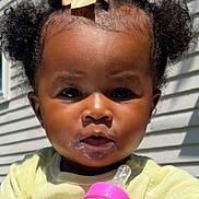 Amara joined the competition — help win amazing prizes! baby, child, milk_bottle, yellow_bow, curly_hair, outdoor, siding, face, portrait, milk, feeding, holding, cute, infant, person, young_child, sunlight, clothing, pink, expression